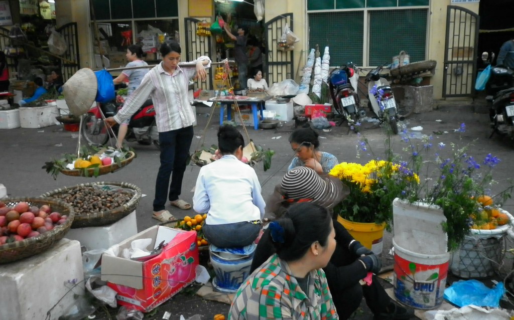 Saleswomen in the Dong Xuan Market in the Old Quarter of Hanoi. One woman balances a shoulder yoke, or "don gahn", full of fresh mangoes.